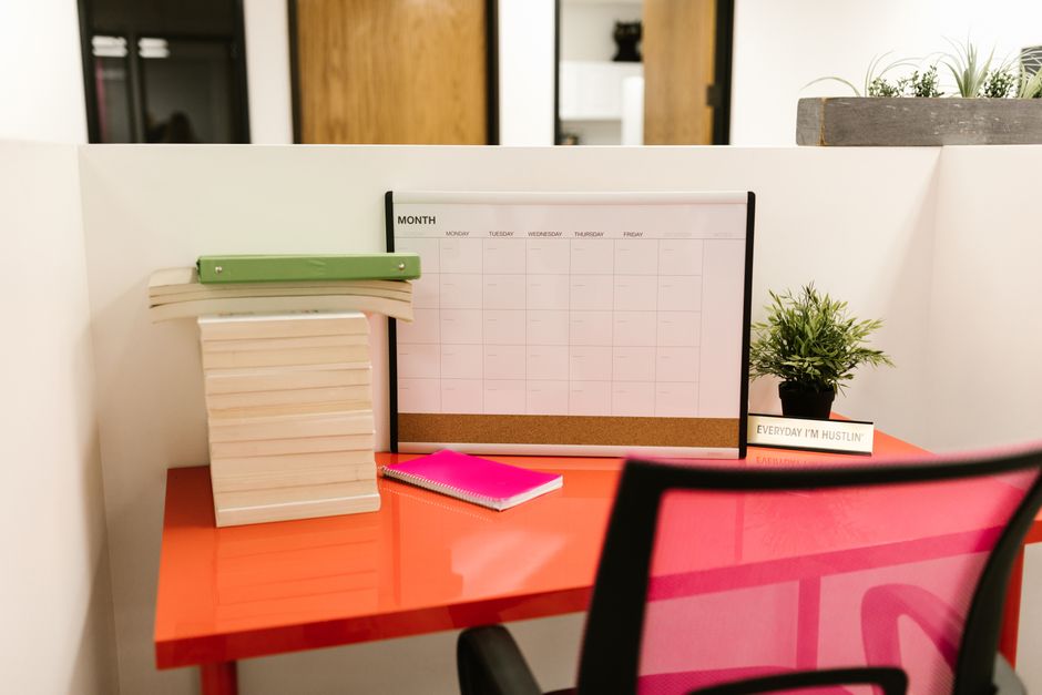 Neat office desk setup featuring a calendar, plant, and vibrant pink chair.